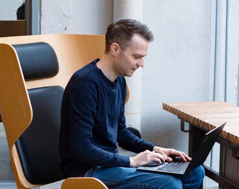 Picture of a person sat in a big lounge chair, looking at his laptop, working
