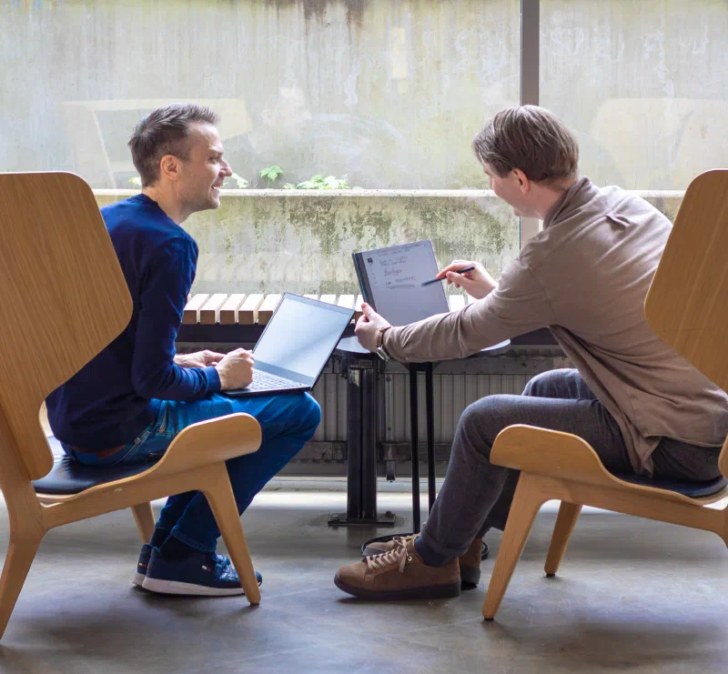 Picture of two people sat in big chairs comparing notes on a laptop and a tablet
